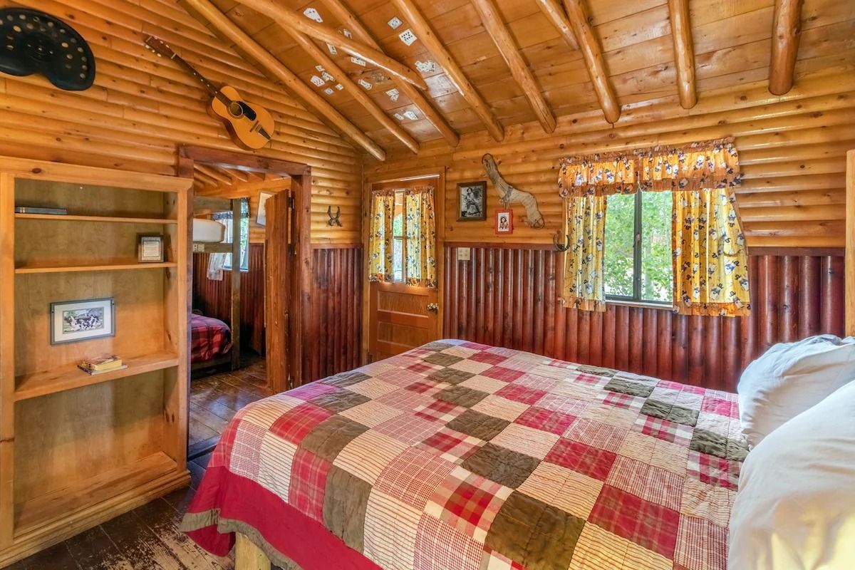 Rustic log cabin bedroom with quilted bed, wooden shelves, and a window view