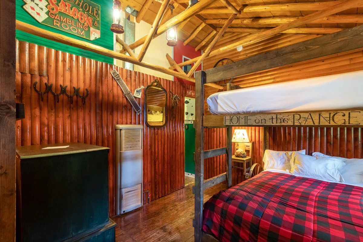Rustic cabin bedroom with a plaid bedspread, wood-paneled walls, and a lofted wooden ceiling