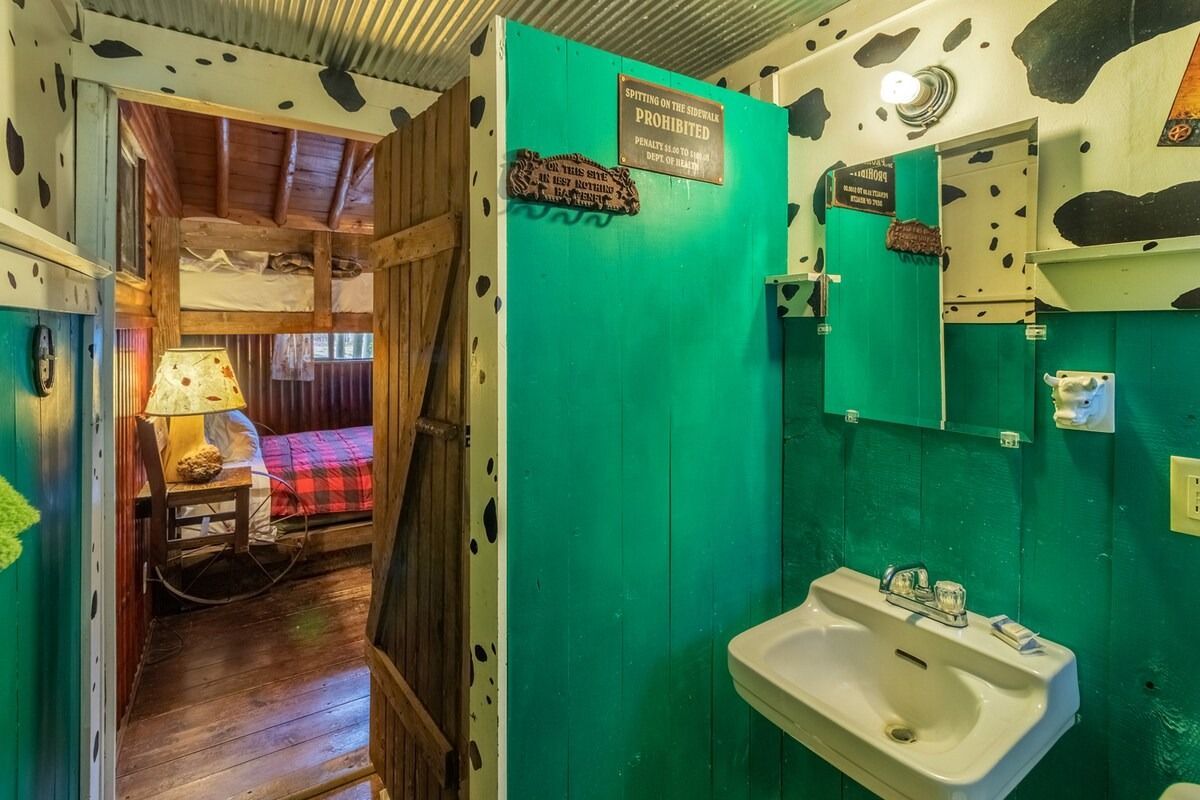 Colorful tiny bathroom with green walls, white sink, and doorway to a cozy wood-paneled room