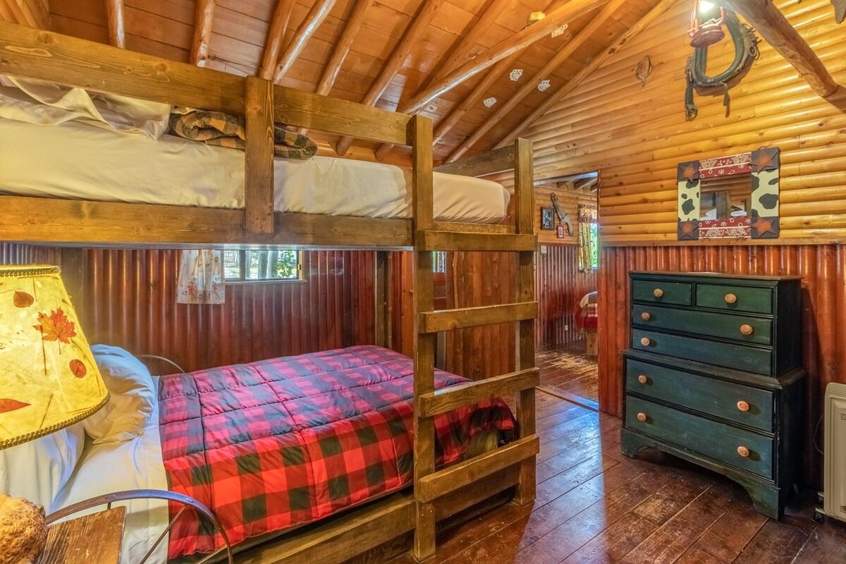 Rustic wood bedroom with bunk bed, red plaid blanket, and blue dresser beneath a slanted ceiling