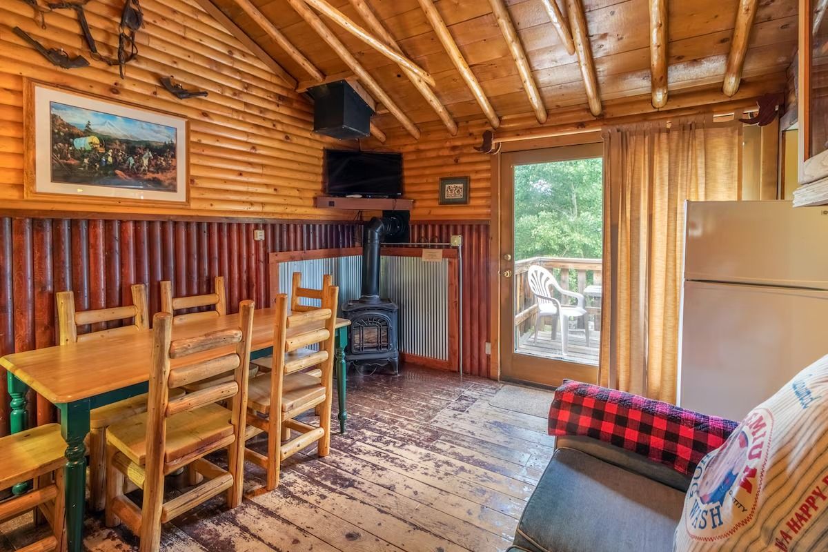 Rustic cabin dining area with wooden table, chairs, wood stove, and sliding glass door to deck