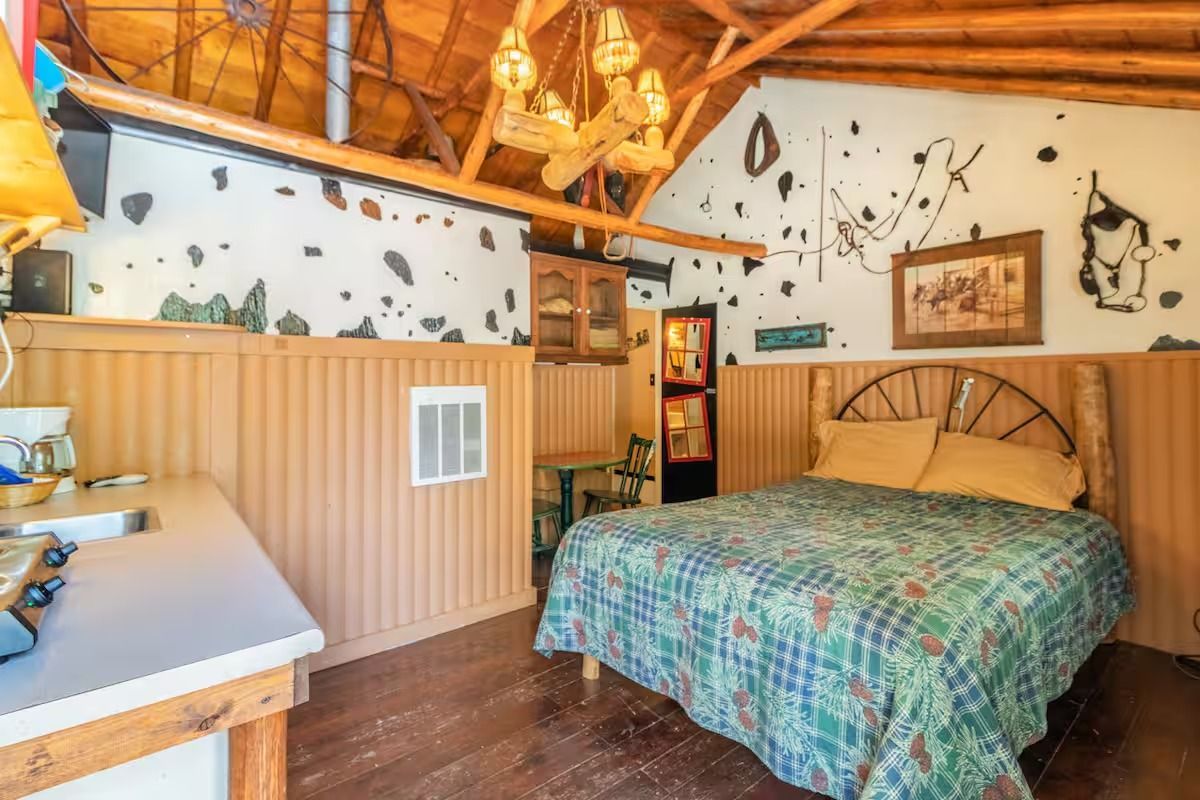 Cozy rustic bedroom with a bed, wood-paneled wall, and vaulted ceiling with exposed beams