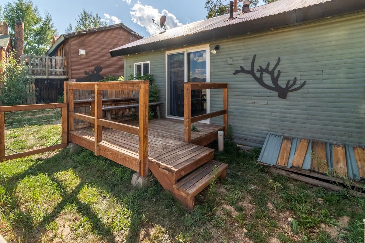 Backyard wooden ramp and small deck beside a house, with fence and lawn in sunlight