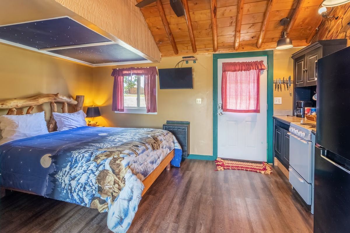 Cozy bedroom with blue bedspread, wood ceiling, small windows, and a door on the far wall