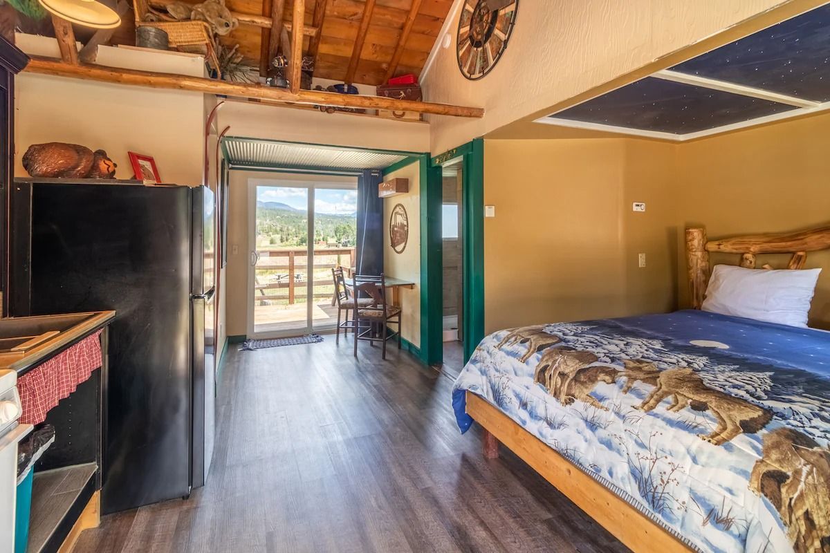 Cozy bedroom with wood floor, patterned bedspread, and open door to a bright outdoor view.