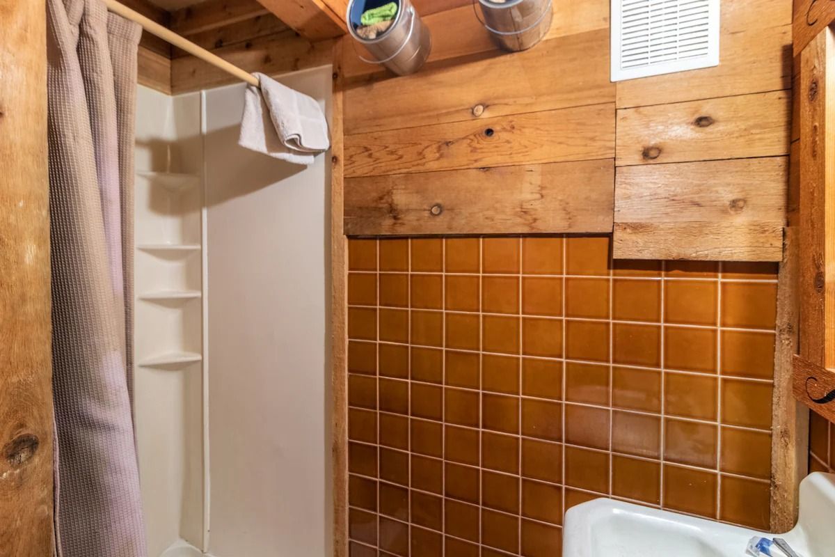Rustic bathroom with wood-paneled walls, brown tile, shower stall, and white sink
