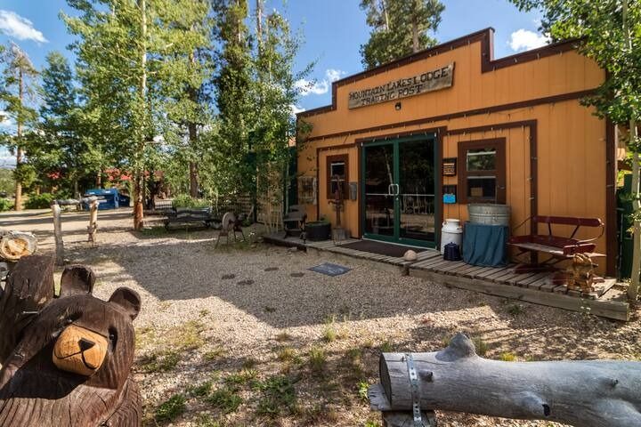 Rustic orange storefront with green trim and outdoor seating in a wooded, sunny setting