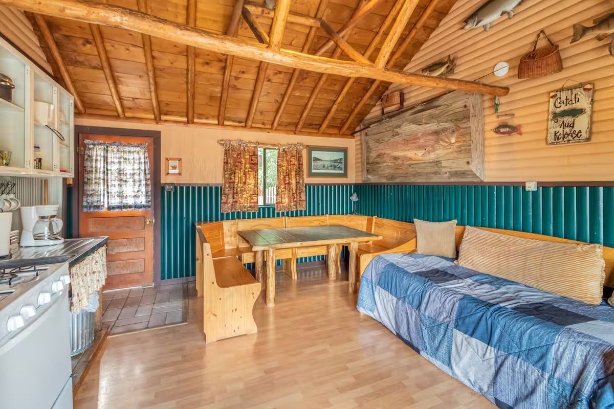 Rustic cabin interior with wood ceiling, blue wainscoting, dining table, and bed-like bench seating