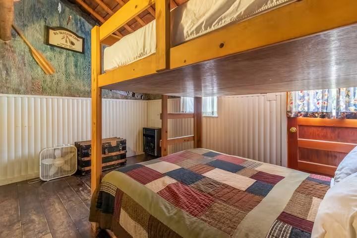 Loft bedroom with a patchwork quilt, wood bunk bed frame, and small window in a cozy cabin room