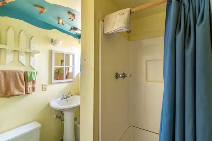 Small bathroom with a shower, sink, towel rack, and blue curtain in yellow and blue decor.