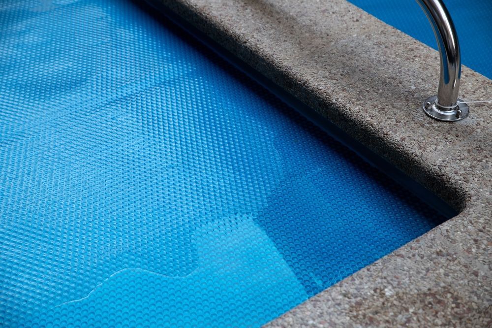 Blue pool water beside a stone pool edge with a metal handrail