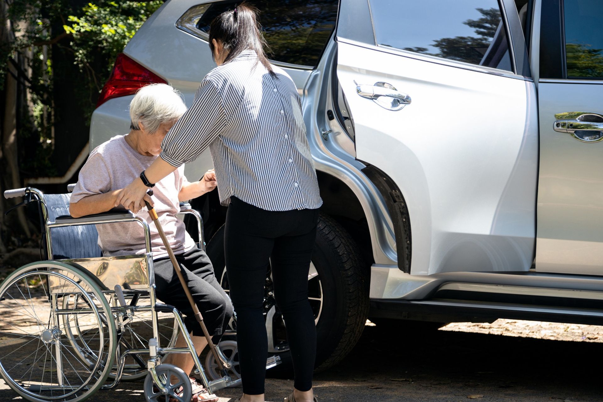 Woman assisting person from wheelchair into a silver SUV.