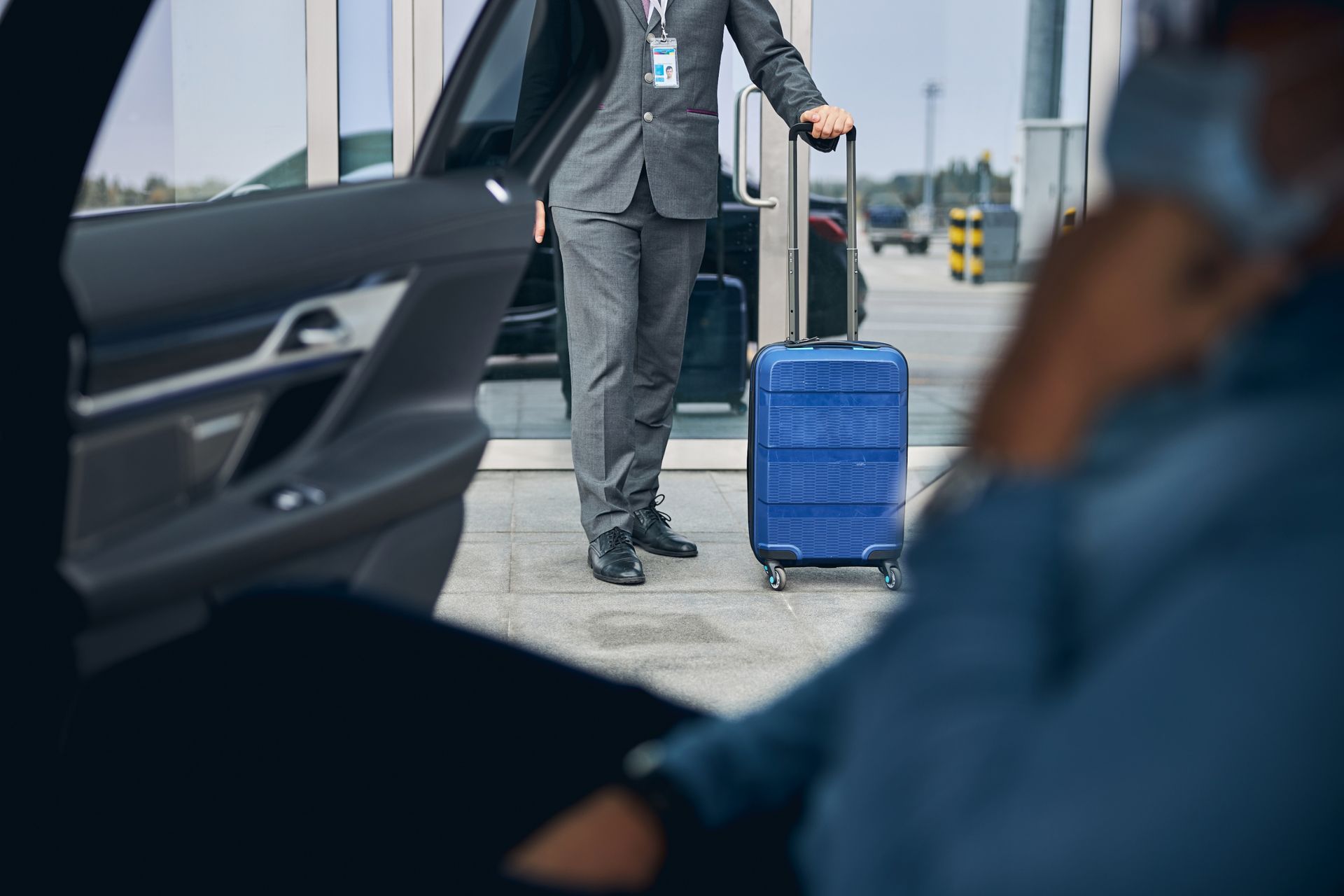 Person exiting car, assistant holding luggage. Airport setting.