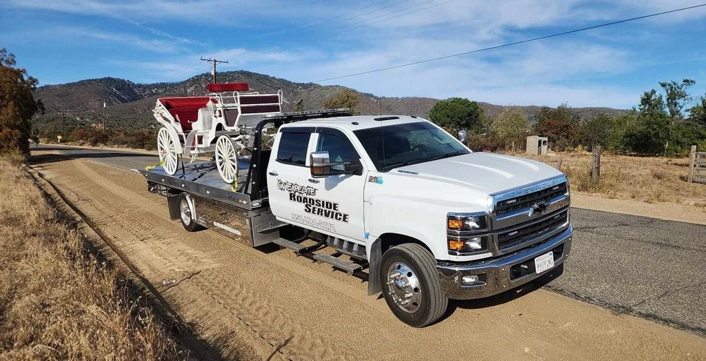 White pickup truck towing a red-and-white trailer on a dirt road in a rural field