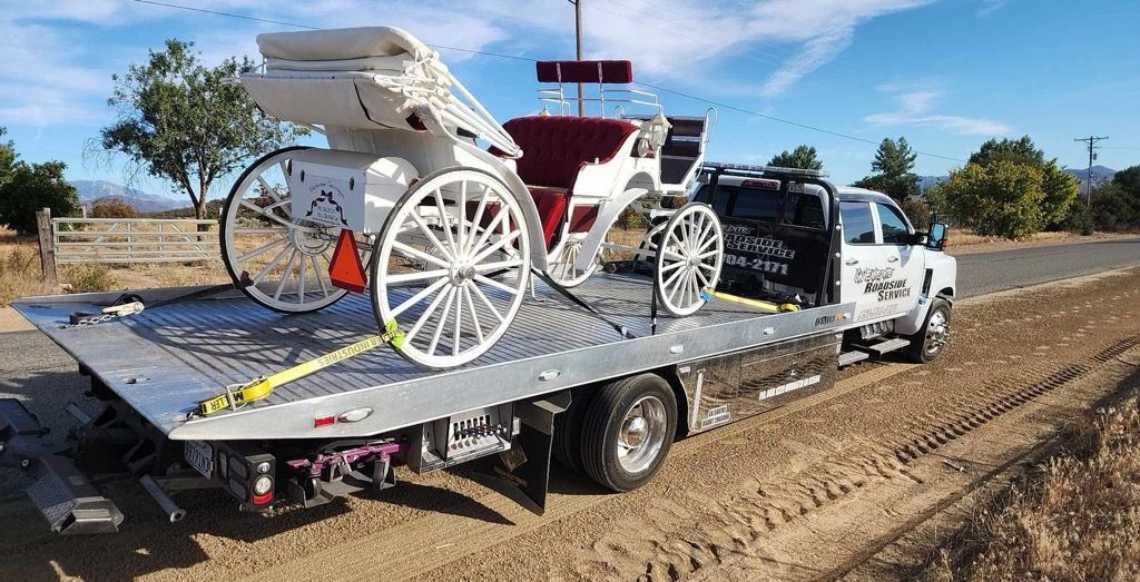 White horse-drawn carriage on a flatbed tow truck in a rural field