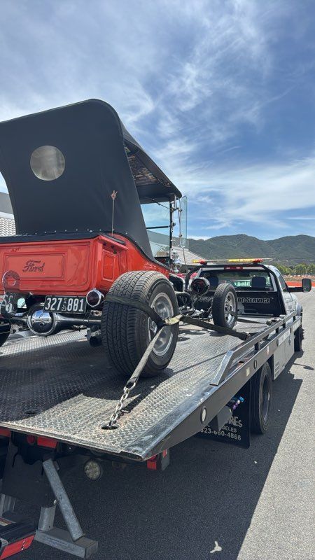 Vintage red-and-black hot rod on a tow truck flatbed under a blue sky