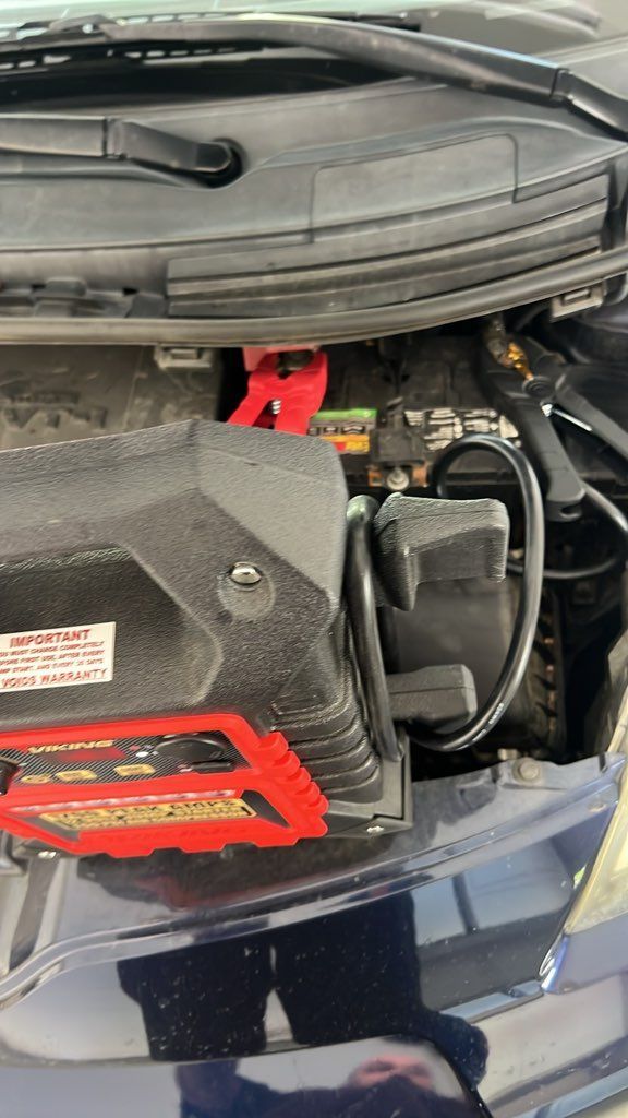 Open car hood showing engine bay with red battery cover and black components
