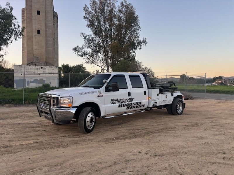 White tow truck parked on dirt near a tall stone tower at dusk
