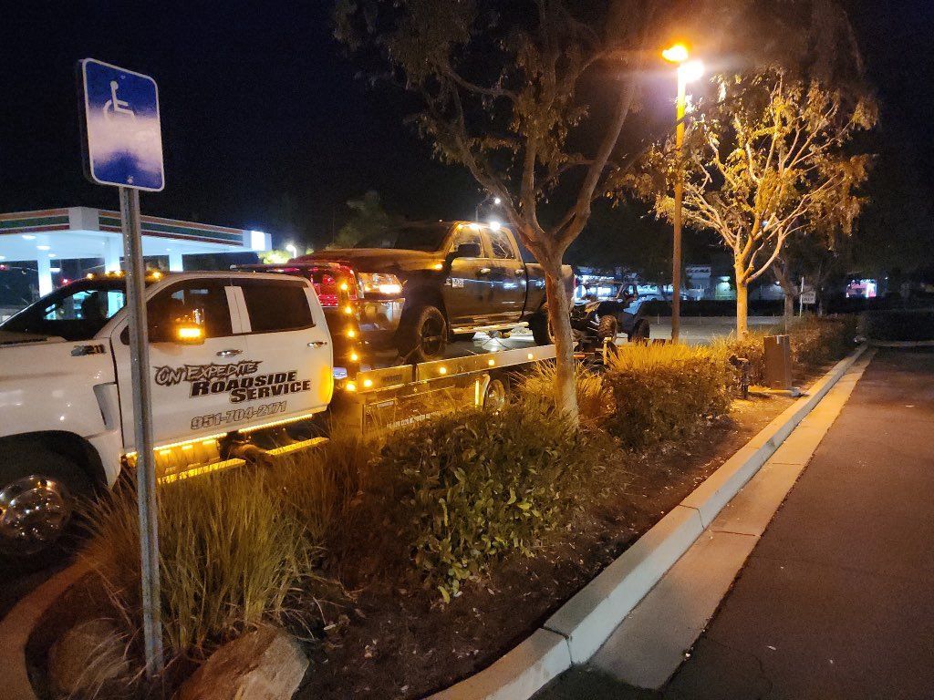 Nighttime parking lot with parked cars, a lit lamppost, and a landscaped median along the curb.