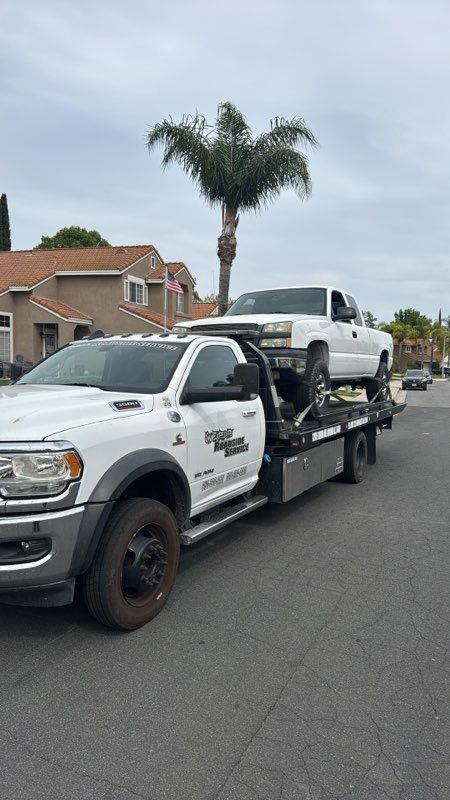 Tow truck hauling a white pickup on a residential street with palm trees
