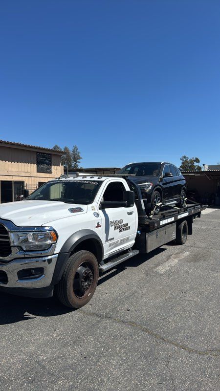 White tow truck carrying a black SUV on a flatbed in a parking lot under a clear blue sky