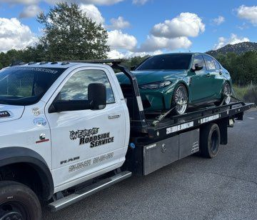 Tow truck carrying a teal sedan on a flatbed trailer beside a white service truck on a road