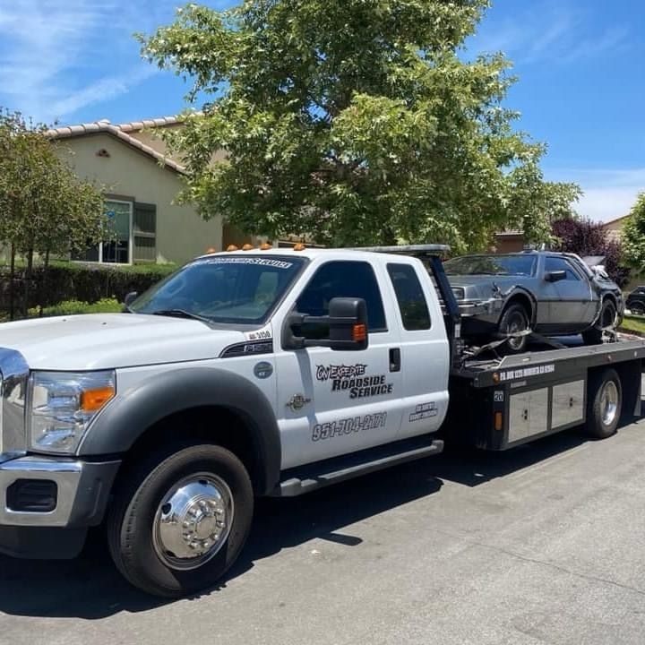 White tow truck hauling a dark sedan on a flatbed in a sunny suburban neighborhood