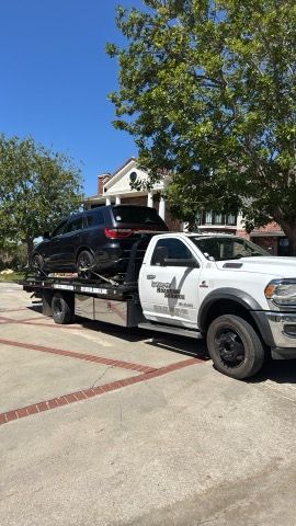 Tow truck hauling a black SUV on a sunny residential street