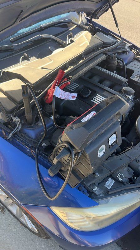 Blue car with hood open, jump starter attached to the engine compartment