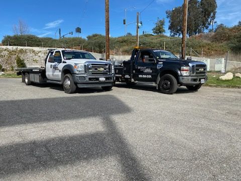 Two tow trucks parked side by side on a sunny gravel lot