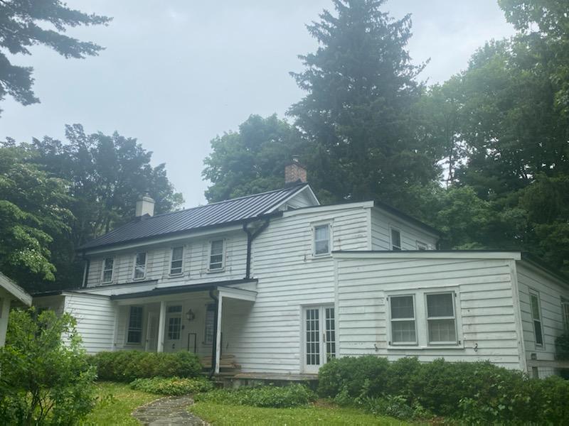 A white house with a black roof is surrounded by trees
