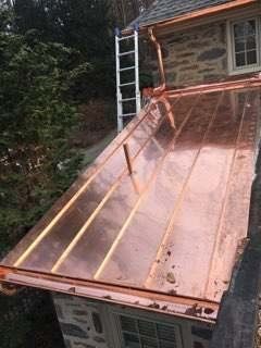 A copper roof is being installed on the side of a house.