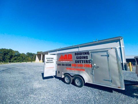 A trailer for roofing siding gutters is parked in a gravel lot.