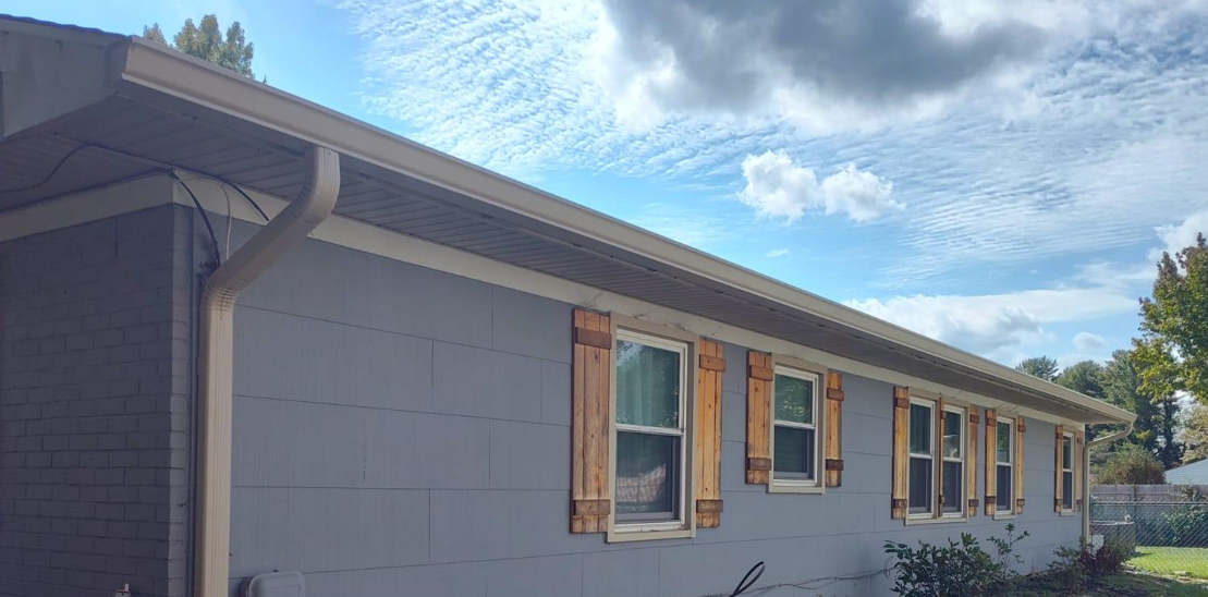 A mobile home with a gutter and shutters on the windows.