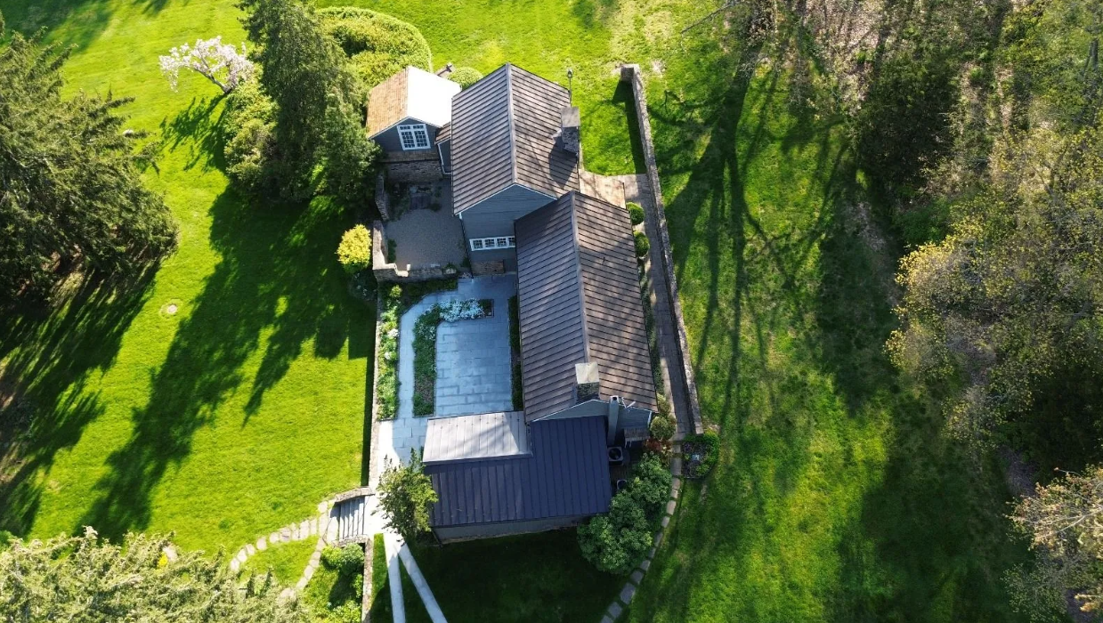 An aerial view of a house in the middle of a lush green field surrounded by trees.