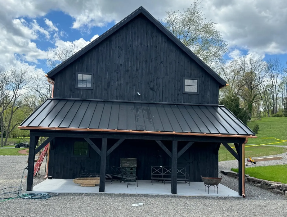 A black barn with a copper roof and a porch.