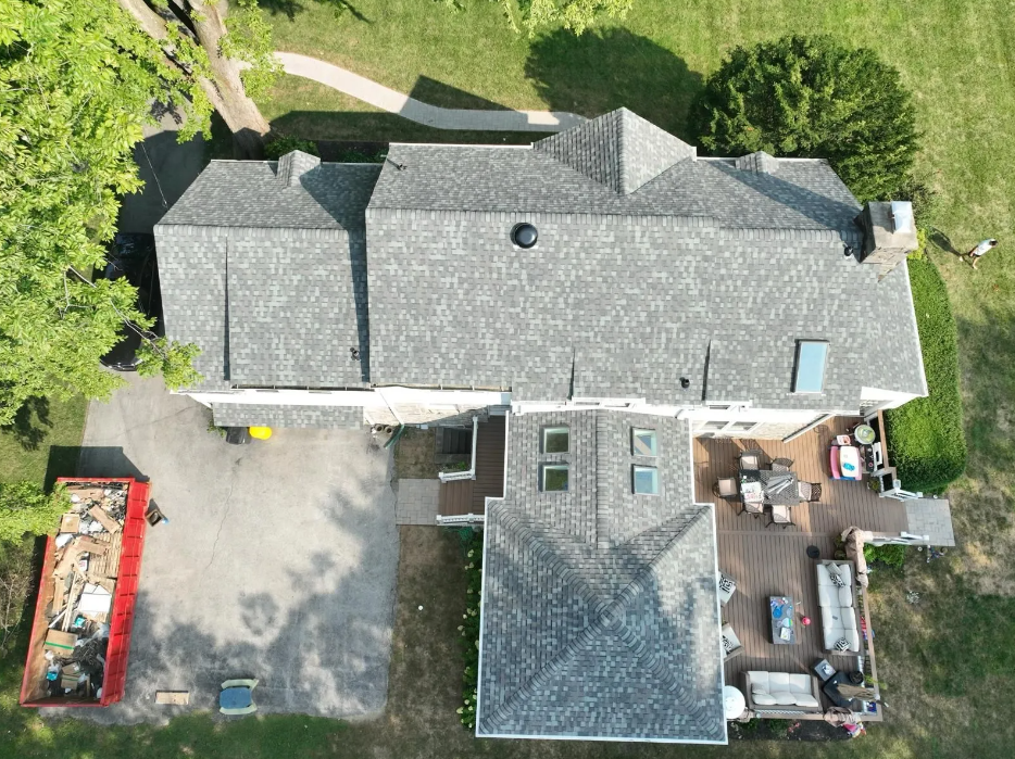 An aerial view of a large house with a gray roof and a red dumpster in front of it.