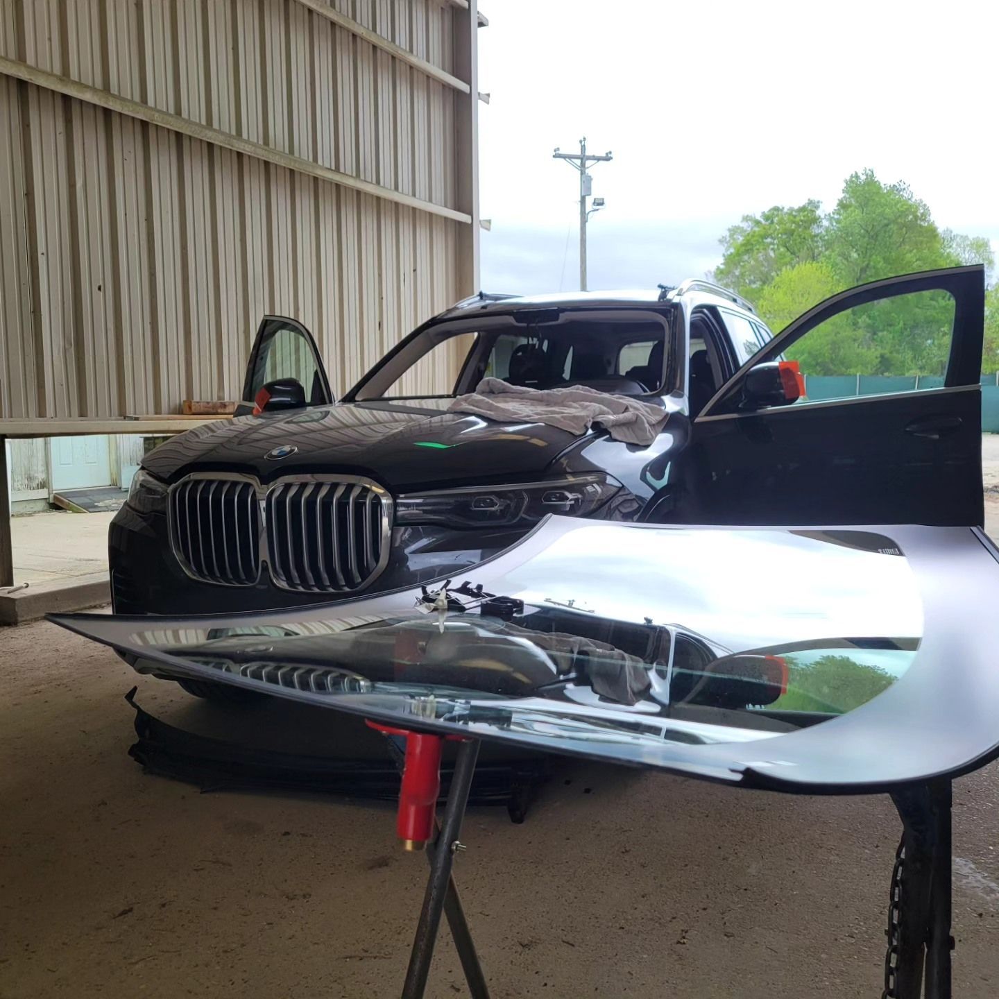 Damaged black SUV with open doors and a detached hood in a repair shop.