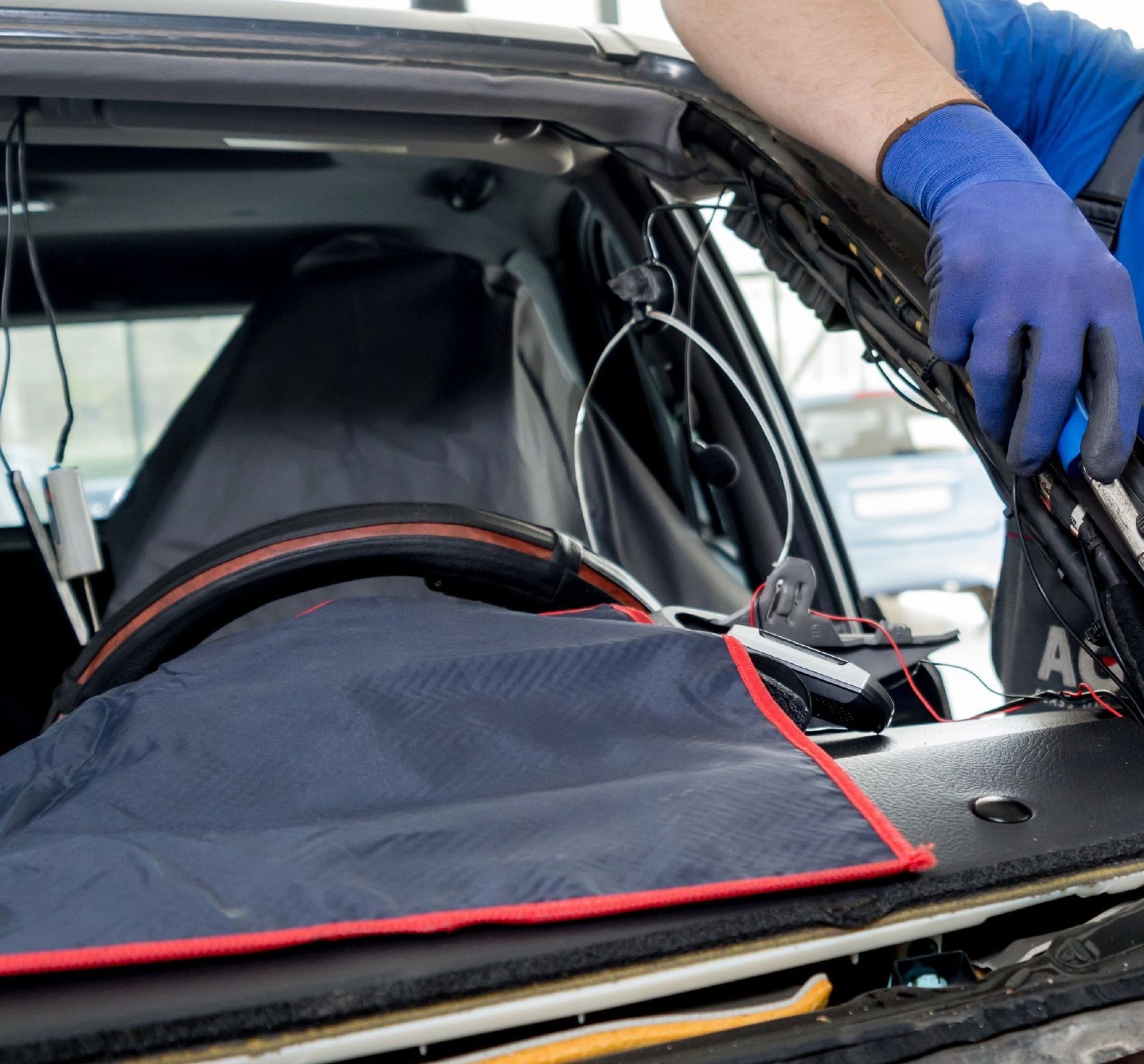 Person in blue gloves working on a car windshield, using tools and covering the dashboard.