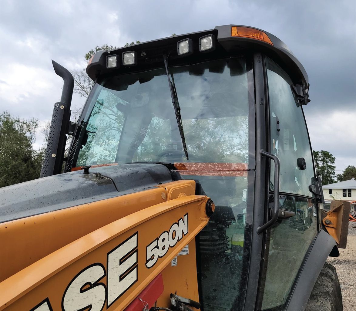 Orange and black Case 580N backhoe, cab with lights, overcast day.