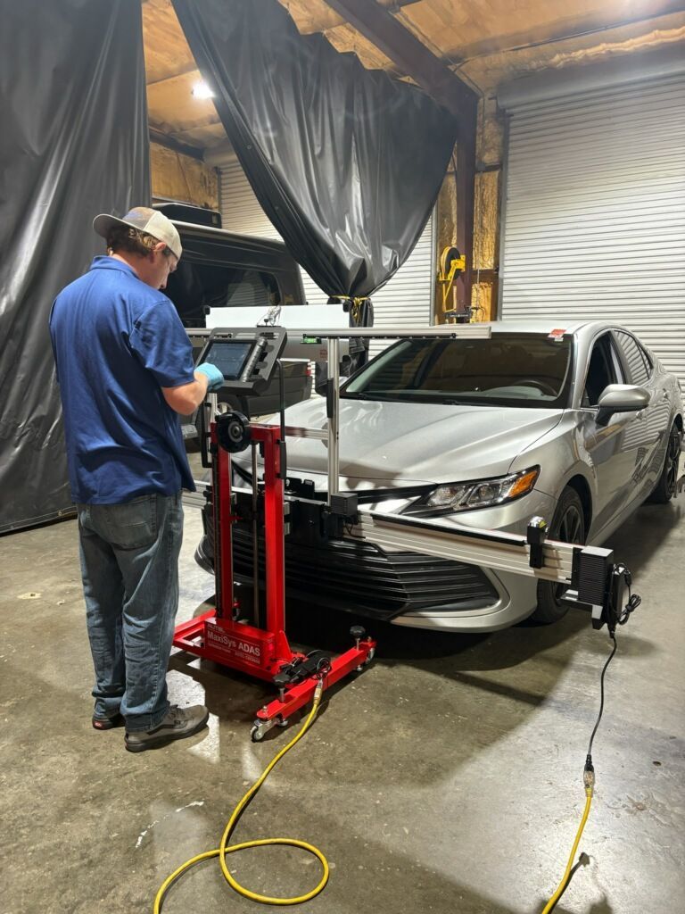 White car's side mirror reflects a garage interior with alignment equipment and tools.