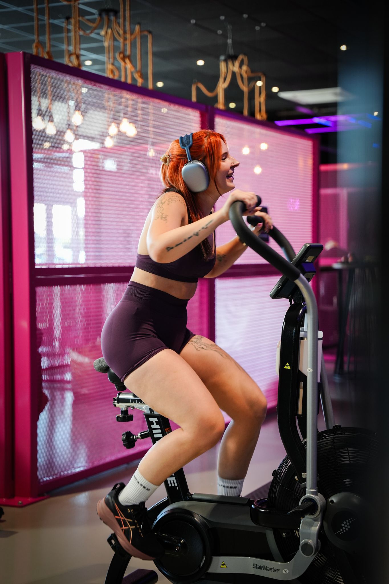 Een sportschool vol met fitnessapparatuur en paarse lichten.