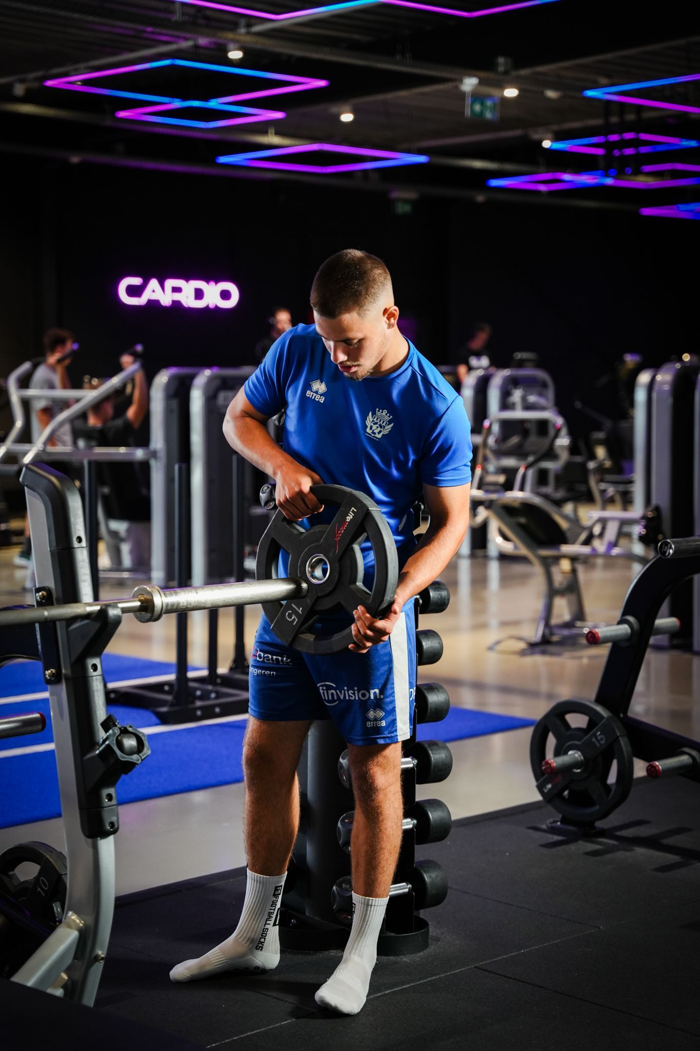 Een sportschool met veel fitnessapparatuur en een neonreclame met de tekst 'kracht'.
