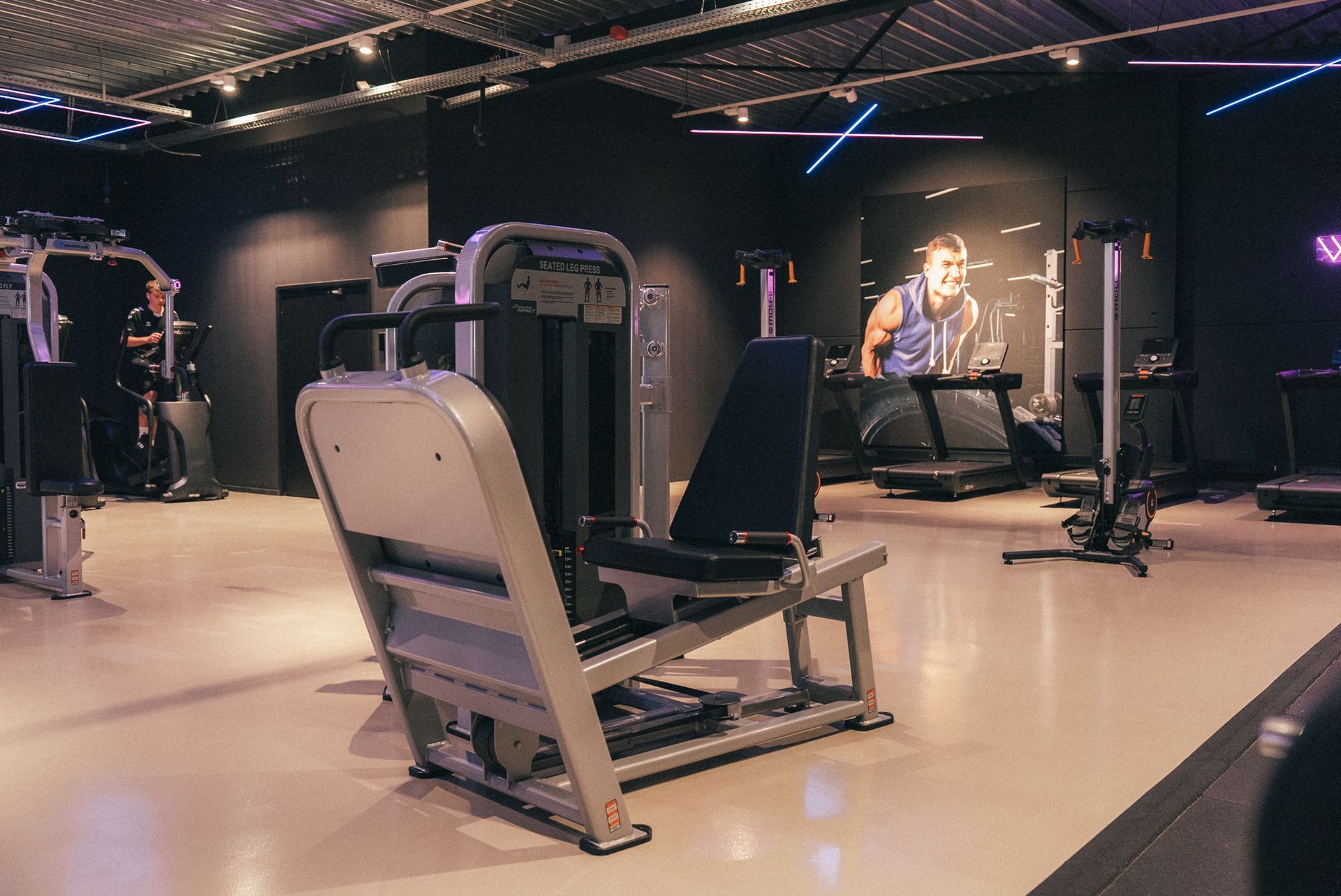 Een sportschool vol met fitnessapparatuur en paarse lichten.