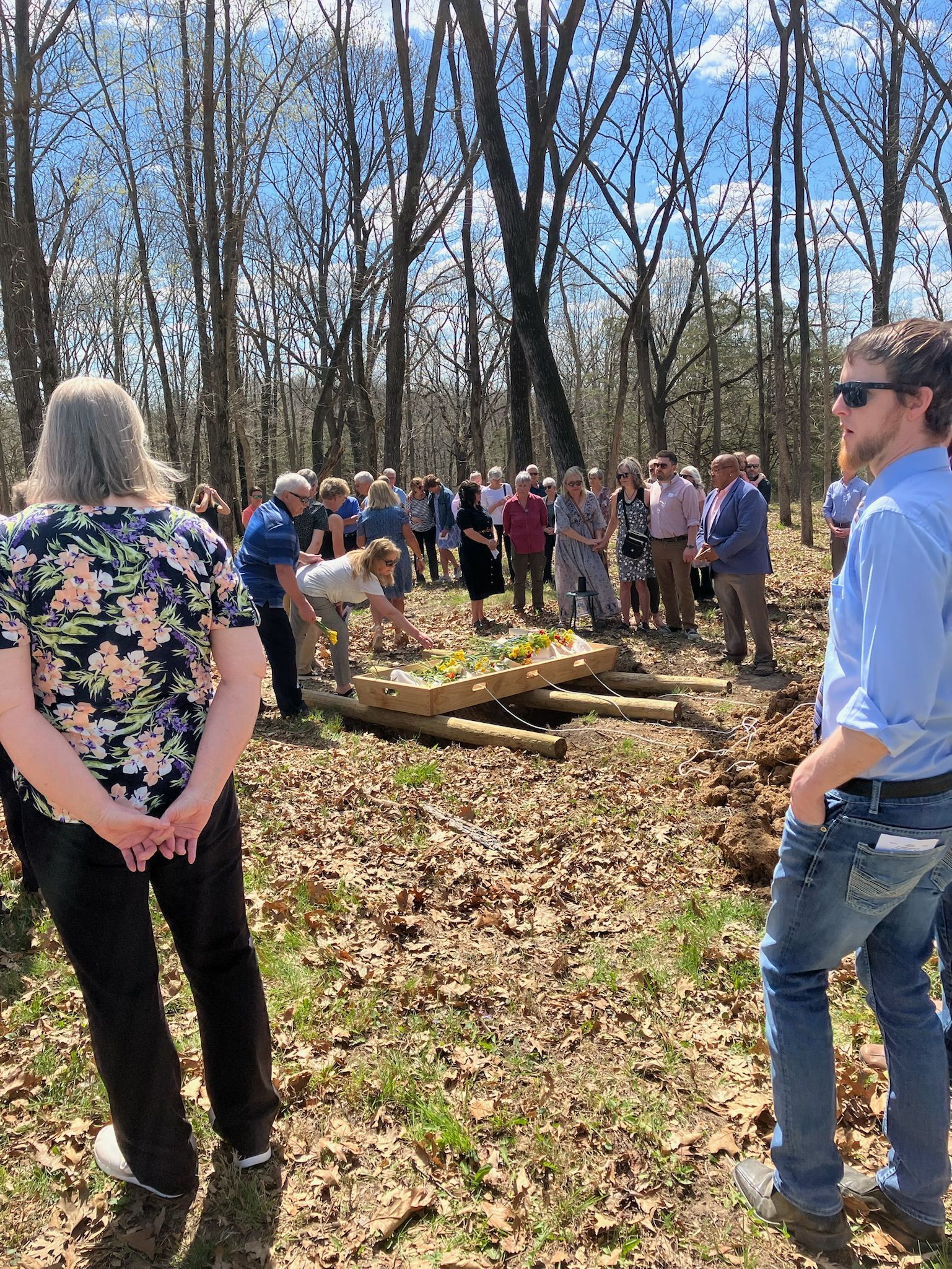 A group of people are standing in the woods talking to each other.