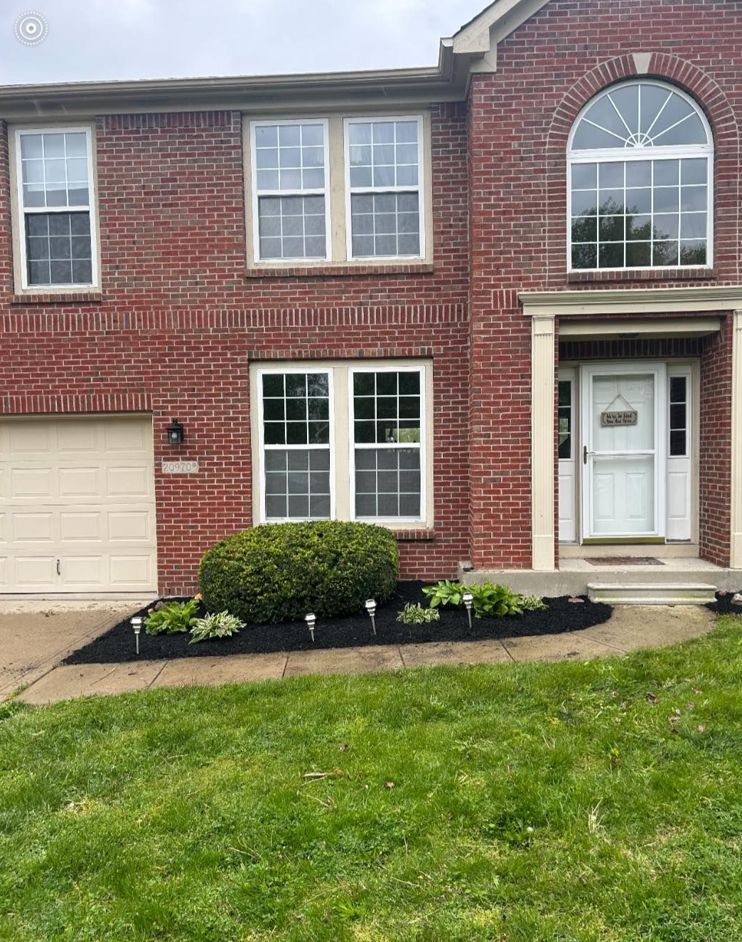 Red brick house with white trim, arched window, and landscaped front yard.