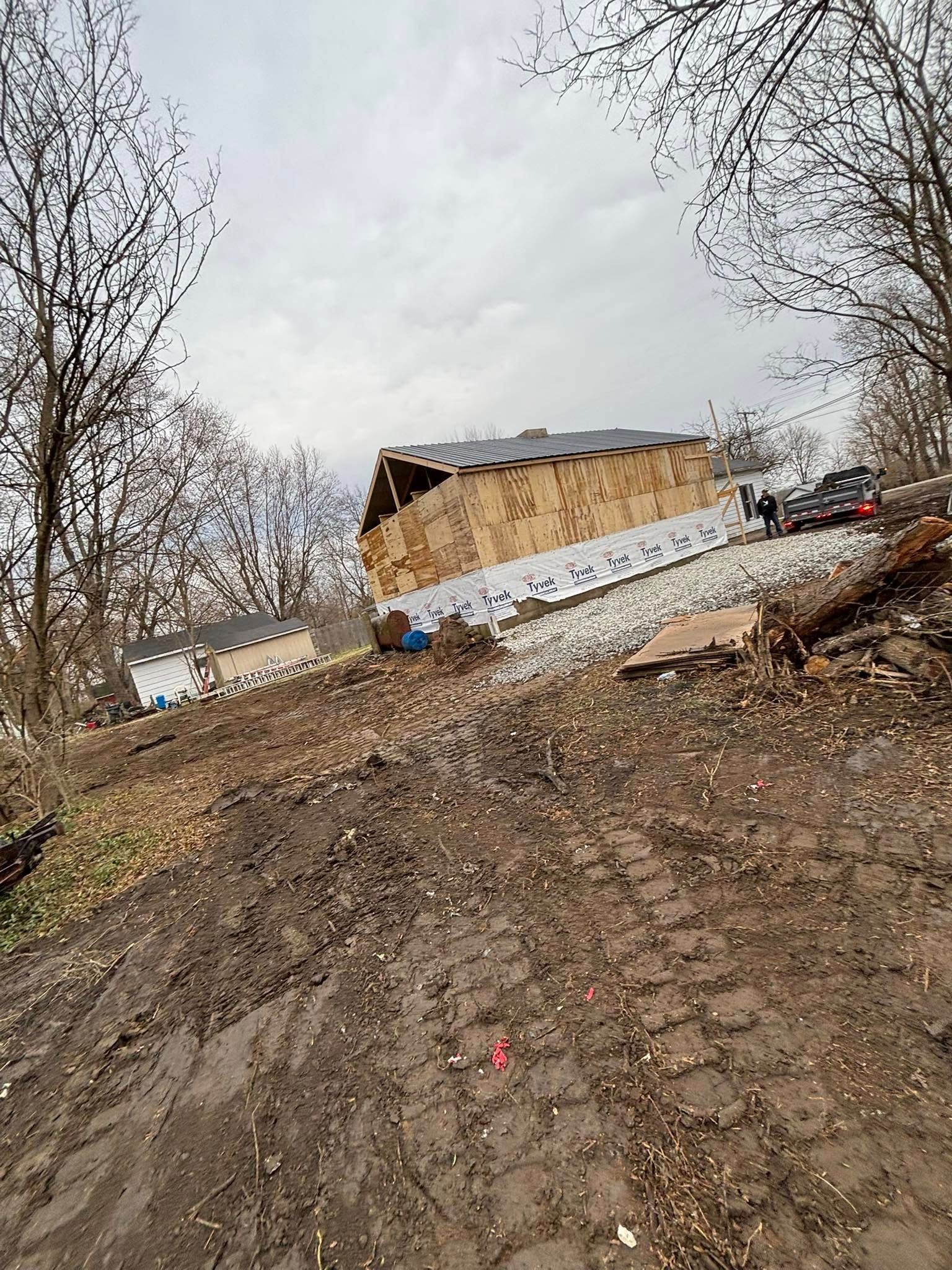 Dirt path leading uphill to a building under construction; a car and two figures are present.
