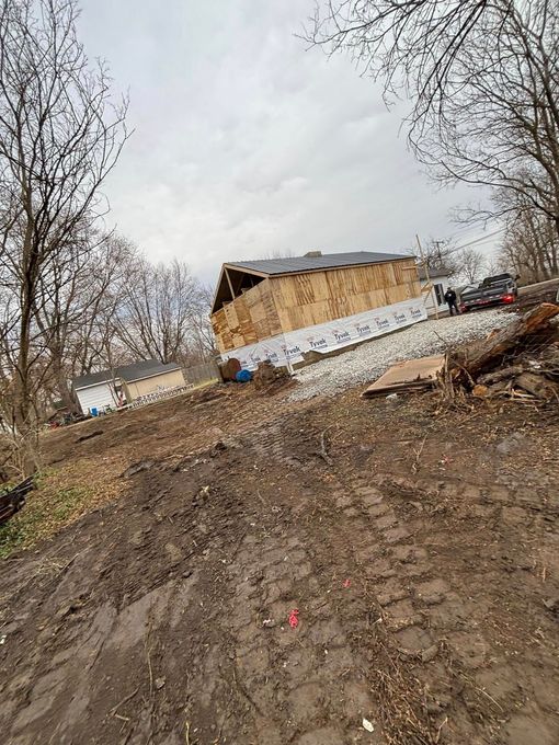 Dirt path leading uphill to a building under construction; a car and two figures are present.