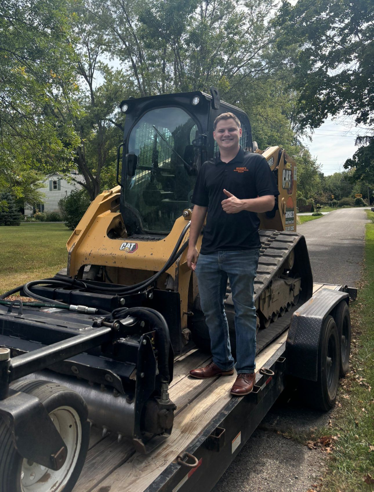 Man giving a thumbs up, standing on a trailer with a yellow track loader.