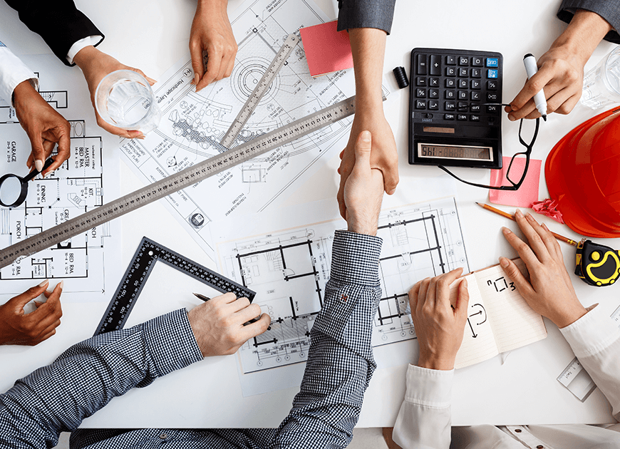Hands shaking over architectural blueprints on a white table; collaborative work environment.
